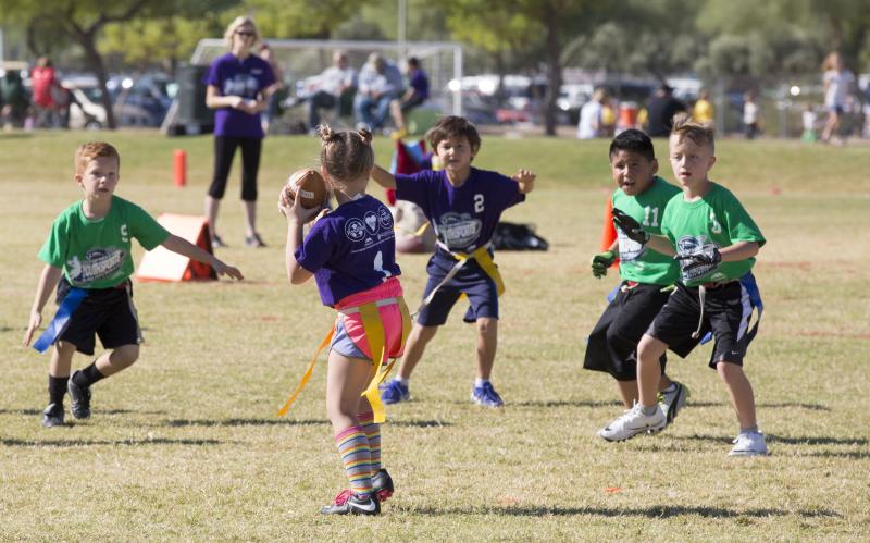 Photo of kids playing co-ed flag football. A girl quarterback is trying to throw the ball to boys